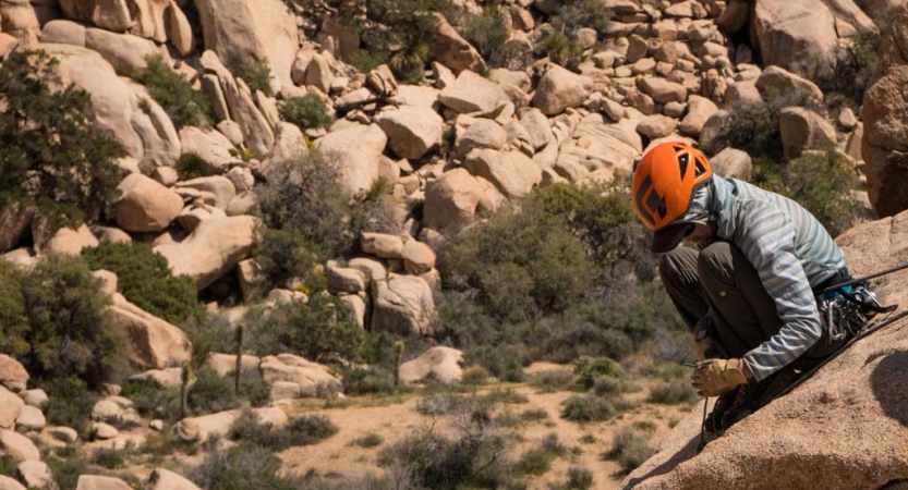 a person wearing a helmet sits on a rock high above a mountainous landscape